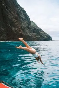 Girl Diving into Ocean with Kauai's Na Pali Coast in background